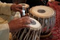 Udit Pankhania tunes his Tabla. The skin is tensioned by a number of cords that run down the sides; inside each pair of cords is a large wooden toggle. The further down the barrel of the drum the toggle is moved, the tighter the skin is made, raising the pitch.\n\nThe black circles in the middle of each drum skin, which enable an even wider variety of sounds to be made, are built up in layers of rice starch mixed with coal dust.