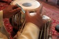 Udit Pankhania tunes his Tabla. The skin is tensioned by a number of cords that run down the sides; inside each pair of cords is a large wooden toggle. The further down the barrel of the drum the toggle is moved, the tighter the skin is made, raising the pitch.\n\nThe black circles in the middle of each drum skin, which enable an even wider variety of sounds to be made, are built up in layers of rice starch mixed with coal dust.