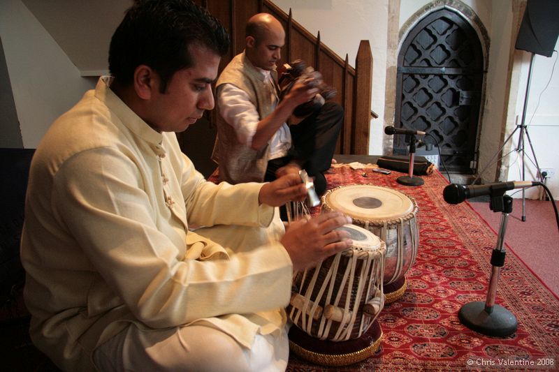 Udit Pankhania tunes his Tabla. The skin is tensioned by a number of cords that run down the sides; inside each pair of cords is a large wooden toggle. The further down the barrel of the drum the toggle is moved, the tighter the skin is made, raising the pitch.\n\nThe black circles in the middle of each drum skin, which enable an even wider variety of sounds to be made, are built up in layers of rice starch mixed with coal dust.